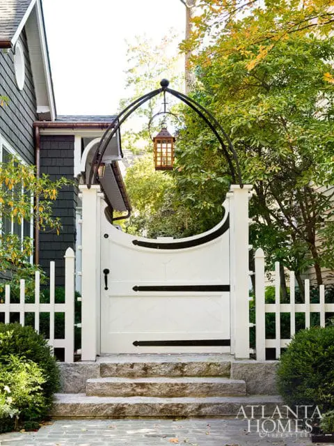 White arched gate with black hardware, stone steps, and picket fence