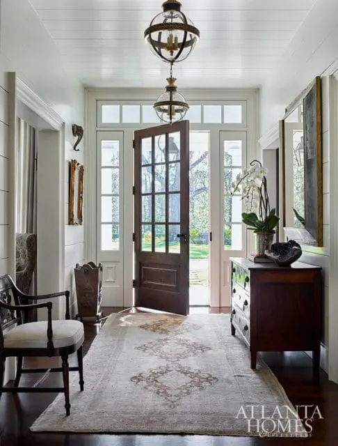 Entryway with open wooden door, two globe pendant lights, patterned rug, and antique chest.
