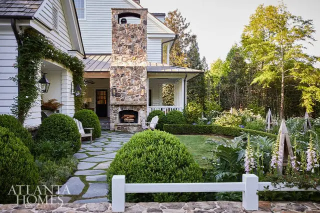 Stone fireplace on white house with climbing roses, flagstone path, and lush garden.