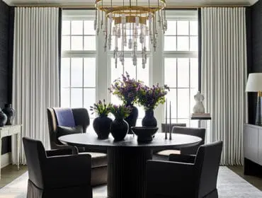 Dining room with dark walls, white curtains, round table, and modern chandelier.