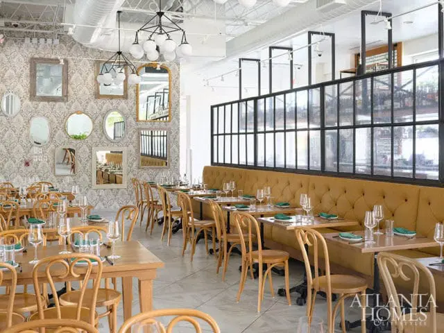 Restaurant dining room with tufted mustard banquettes, wood tables, and patterned wallpaper