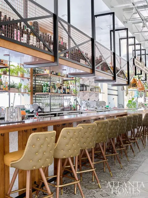 Bar with tufted olive green stools and a wooden counter, wine bottles on upper shelves.