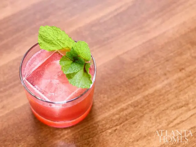Pink cocktail with ice and mint garnish on a wooden surface.