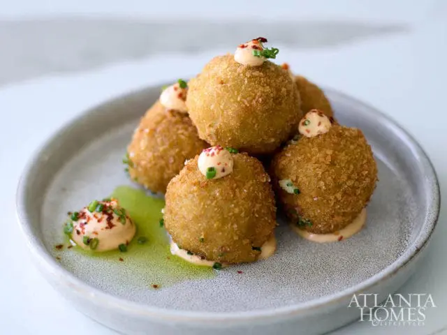 Fried croquettes topped with sauce and chives on a gray plate with green sauce.
