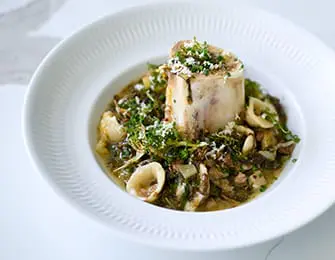 Bone marrow served with pasta and greens in a white bowl