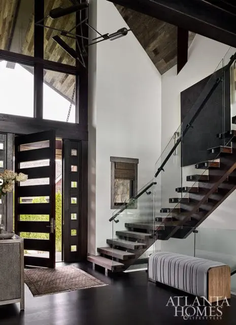 Entryway with open wood doors, floating wood stairs with glass railings, and gray bench.