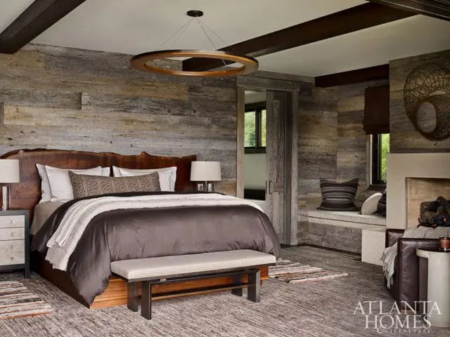 Bedroom with wood plank walls, live-edge headboard, circular pendant light, and stone fireplace.