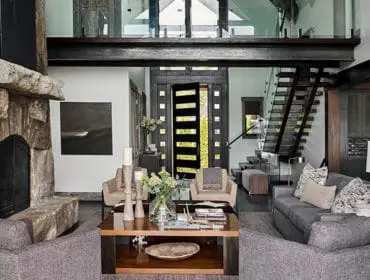 Living room with stone fireplace, gray sofas, and modern staircase