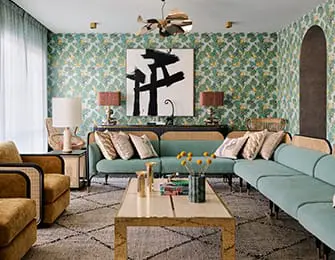 Living room with teal sectional sofa, gold armchairs, patterned wallpaper, and abstract art