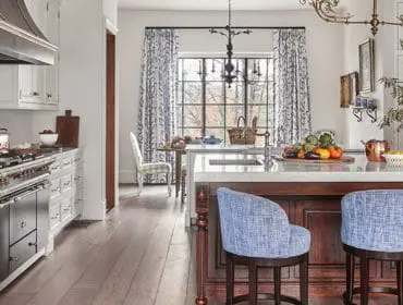 White kitchen with marble island, blue upholstered stools, and copper accents.