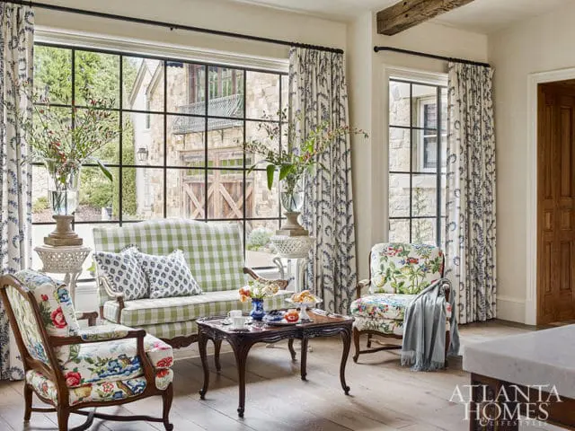 Living room with floral armchairs, green gingham sofa, and large windows overlooking stone house
