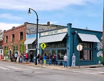 Teal building with white striped awnings and 'LITTLE TART' sign, people outside.