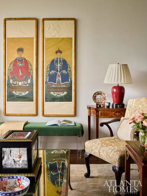 Two framed Asian portraits hang above a green bench with a book. A chair and lamp are nearby.
