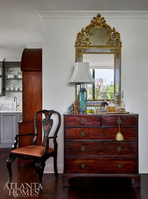 Dark wood dresser with ornate gold mirror above. Chair with black and orange details.
