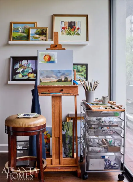 Artist's studio with easel, paintings, art supplies, and a leather stool.