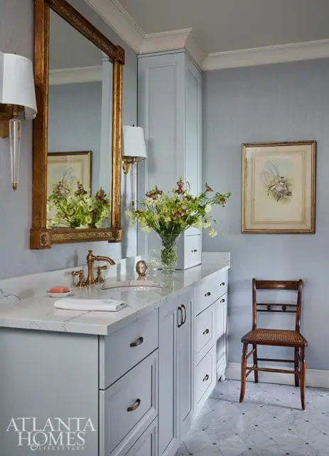 Light blue vanity with marble countertop, brass faucet, and gold mirror.