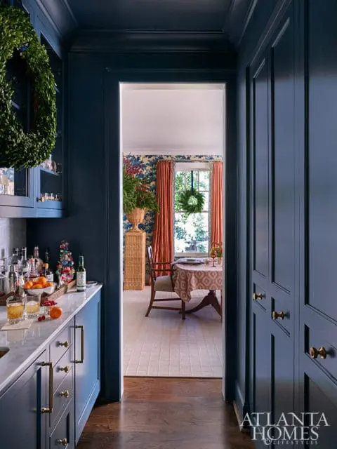 Dark blue kitchen with marble countertops, brass hardware, and a doorway to a dining area.