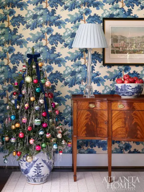 Decorated Christmas tree in blue and white planter, wooden cabinet, and framed artwork