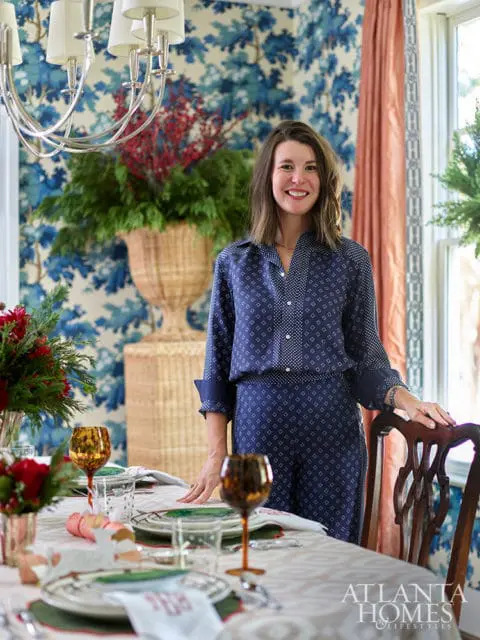 Woman in navy patterned outfit standing by a dining table with blue floral wallpaper and a large