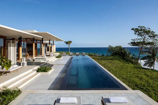 Modern villa with infinity pool overlooking the ocean, featuring white roofs and natural wood