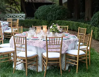Outdoor dining table set with chairs, china, and floral centerpiece on grass