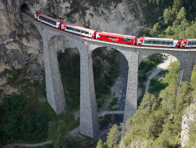Red Glacier Express train crossing a stone viaduct over a gorge with trees