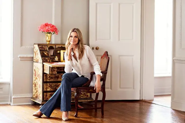 Woman in white shirt and jeans sitting in ornate chair next to antique writing desk