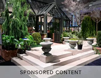 Greenhouse structure with lush plants and urns on stone steps.