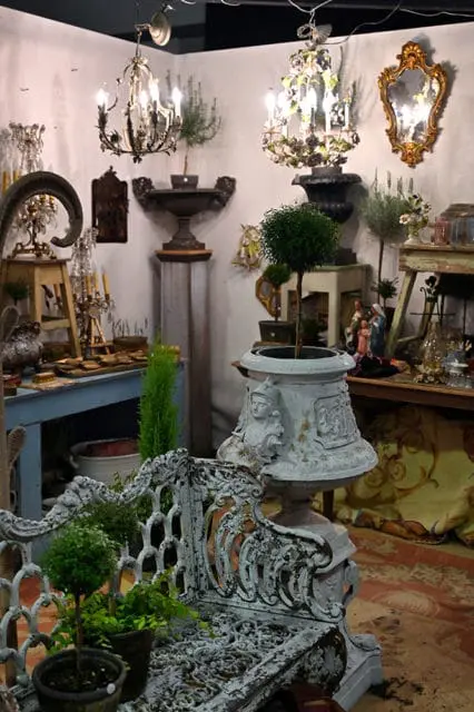 Antique white bench with ornate metalwork, surrounded by decorative urns and chandeliers.