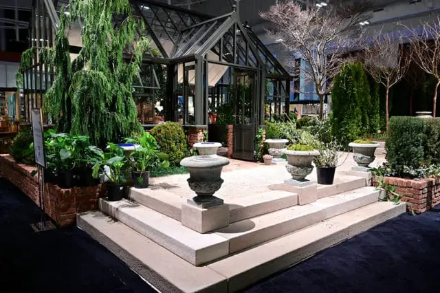 Greenhouse with stone steps, urns, and various plants.