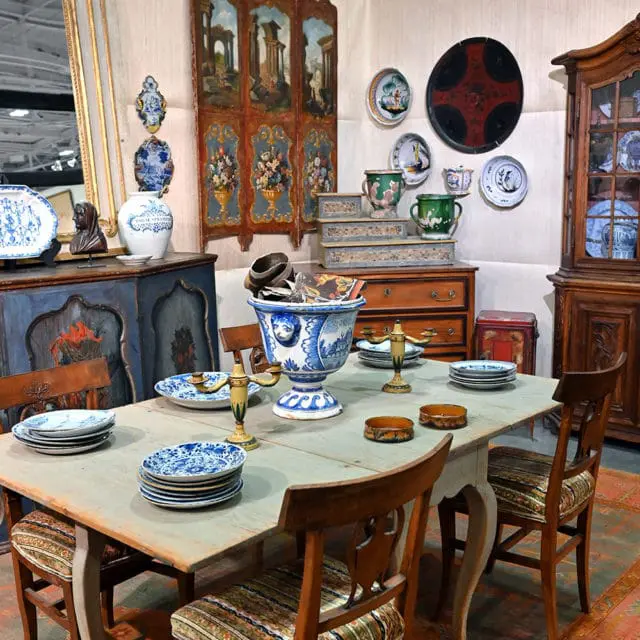 Dining table with blue and white plates, ornate vase, and wooden chairs.