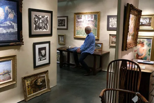 Man in blue shirt sitting on table in art gallery with paintings on walls