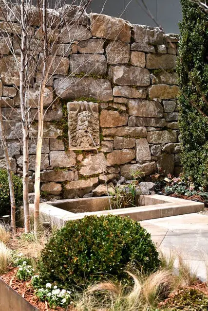 Stone wall with a carved face fountain spilling into a concrete basin