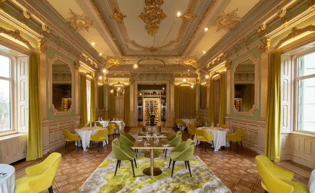 Elegant dining room with ornate gold ceiling, pale green walls, and yellow chairs.