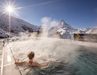 People in hot tub with steam rising, snowy mountains and Matterhorn in background