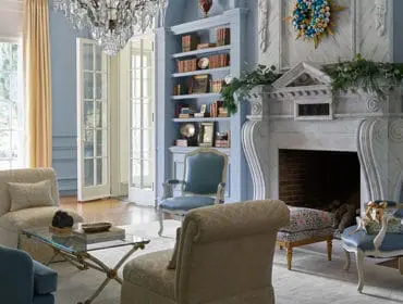 Light blue living room with marble fireplace, built-in bookshelves, and upholstered furniture.
