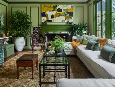 Green living room with white tufted sofa, patterned armchairs, glass coffee table, and abstract art