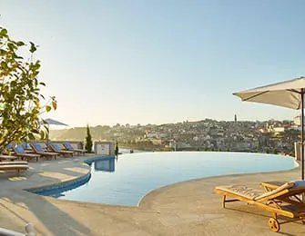 Infinity pool overlooking city skyline with lounge chairs and umbrellas