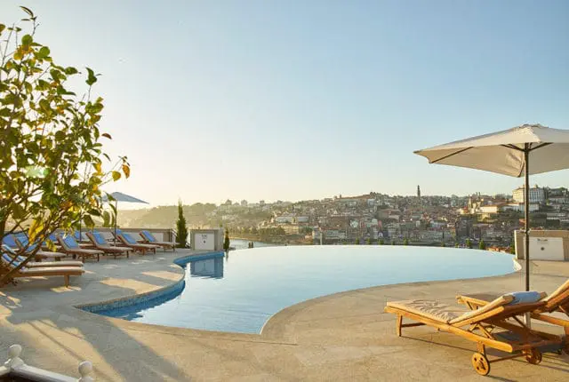 Infinity pool overlooking a city skyline at sunset, with lounge chairs and umbrellas