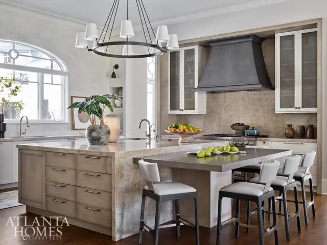 Kitchen island with marble countertop, gray cabinetry, and bar stools. Large window and range hood