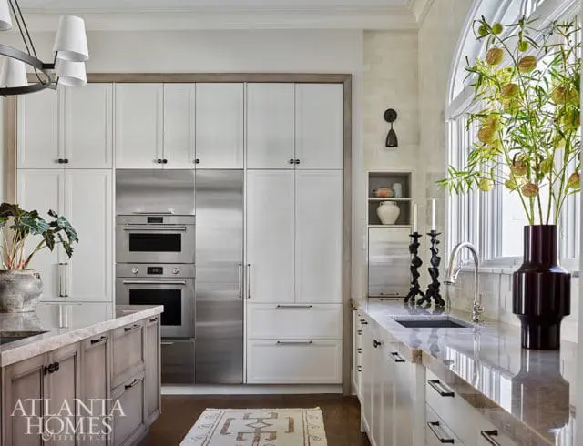 White kitchen with stainless steel appliances, marble countertops, and gray island cabinetry.