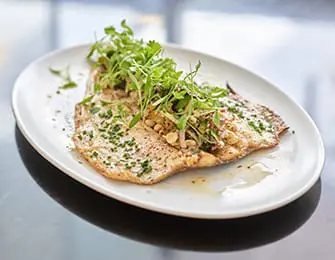 Oval white plate with cooked fish topped with fresh green herbs and chopped nuts