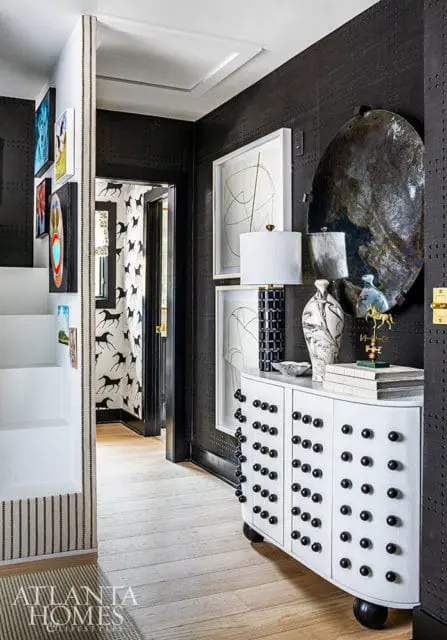 Hallway with black textured wallpaper, white curved cabinet with black knobs, and abstract art.
