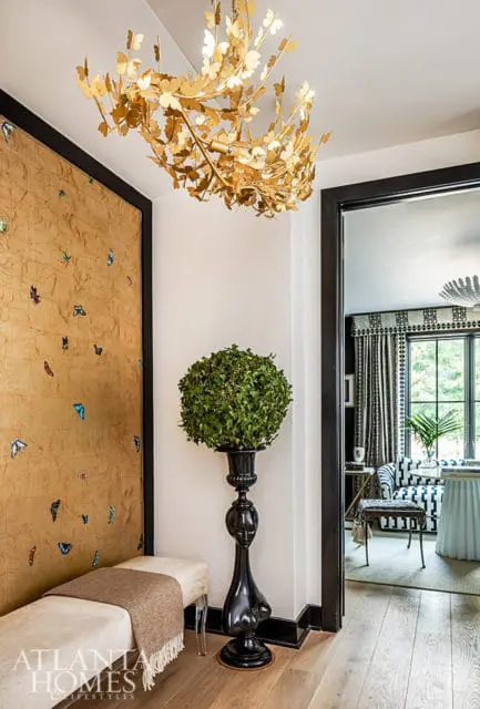 Hallway with gold butterfly chandelier, textured wall, and black sculptural pedestal