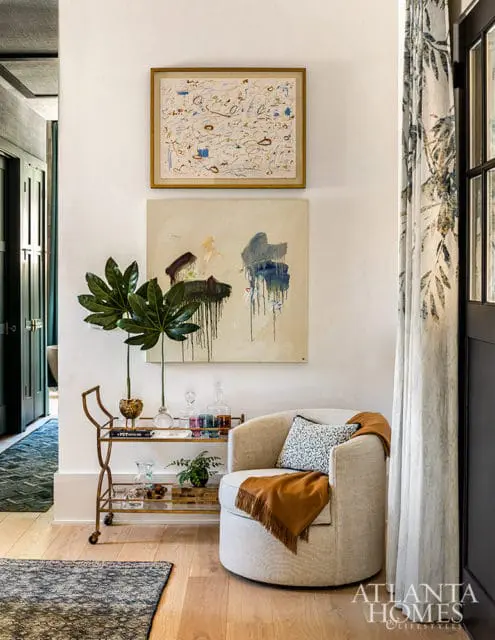 Cream swivel chair with orange throw, abstract art, bar cart, and patterned curtains