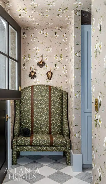 Wingback chair with floral upholstery and brown straps, next to a door and blue cabinet.