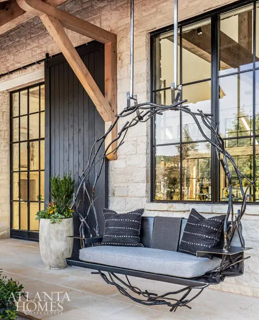 Porch swing with gray cushions and black patterned pillows on stone patio.