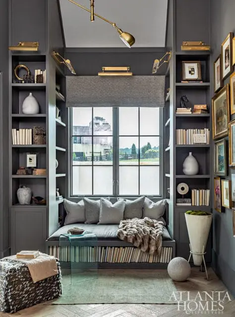 Gray built-in reading nook with bookshelves, plush cushions, and fur throw. Window overlooks a