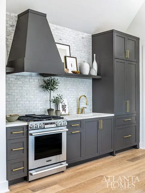 Gray kitchen with stainless steel range, white subway tile backsplash, and gold hardware.