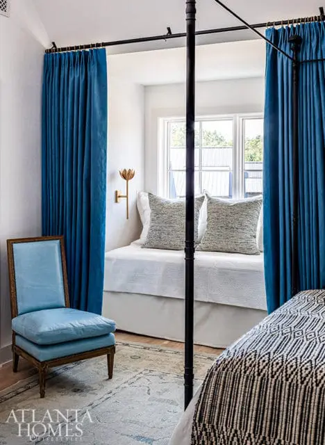 Bedroom with blue velvet curtains, a light blue upholstered chair, and a four-poster bed.